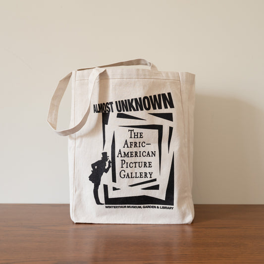 Tote bag with 'Almost Unknown: The African-American Picture Gallery' design on a wooden surface.