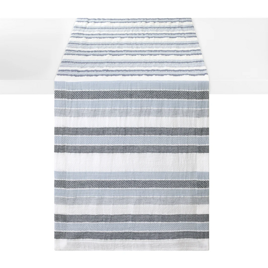 A striped woven cotton table runner with horizontal stripes in shades of blue and white, shown hanging against a white background.