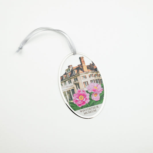 An oval-shaped hanging ornament featuring a printed illustration of the Winterthur Museum building with pink flowers and the text 'WINTERTHUR MUSEUM' at the bottom, suspended by a clear ribbon on a white background.