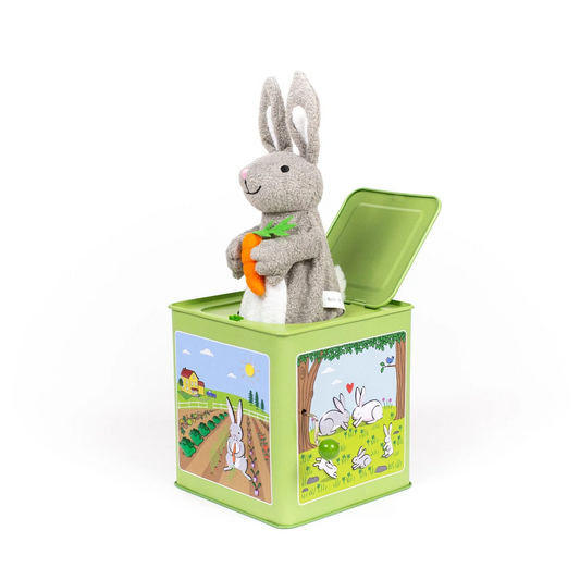 Side view of a green metal jack-in-the-box featuring various bunny pastoral illustrations with a plush gray bunny holding a carrot sticking out of the top.