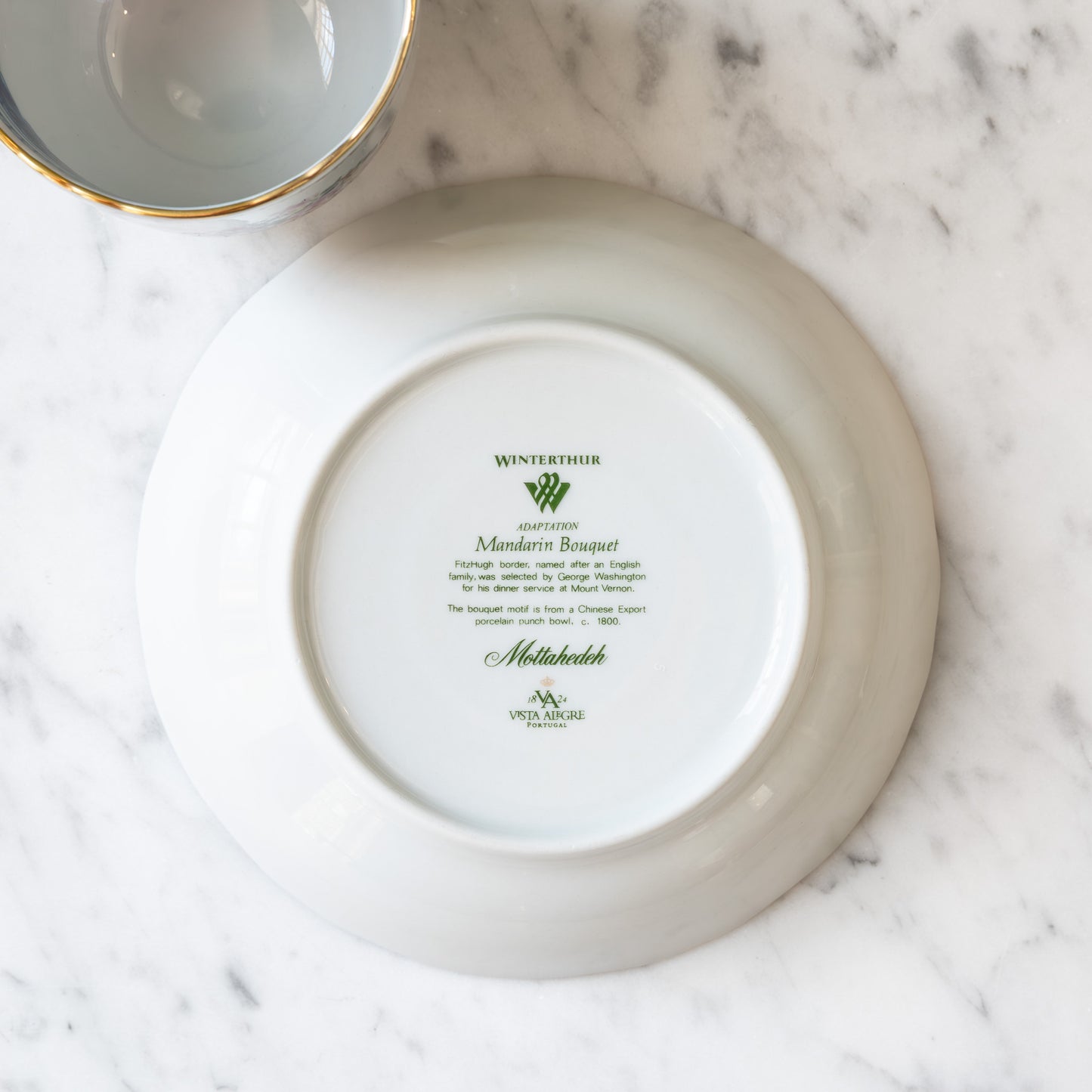 Bottom of a white ceramic saucer with branding on a marble surface.