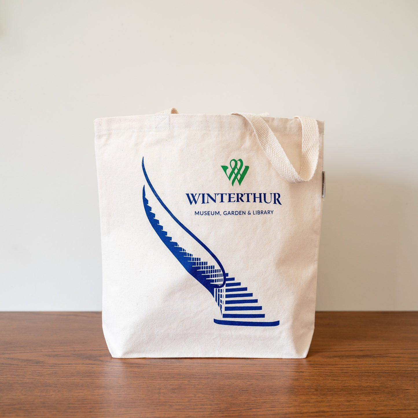 Beige tote bag with blue staircase design and 'Winterthur' logo on a wooden surface