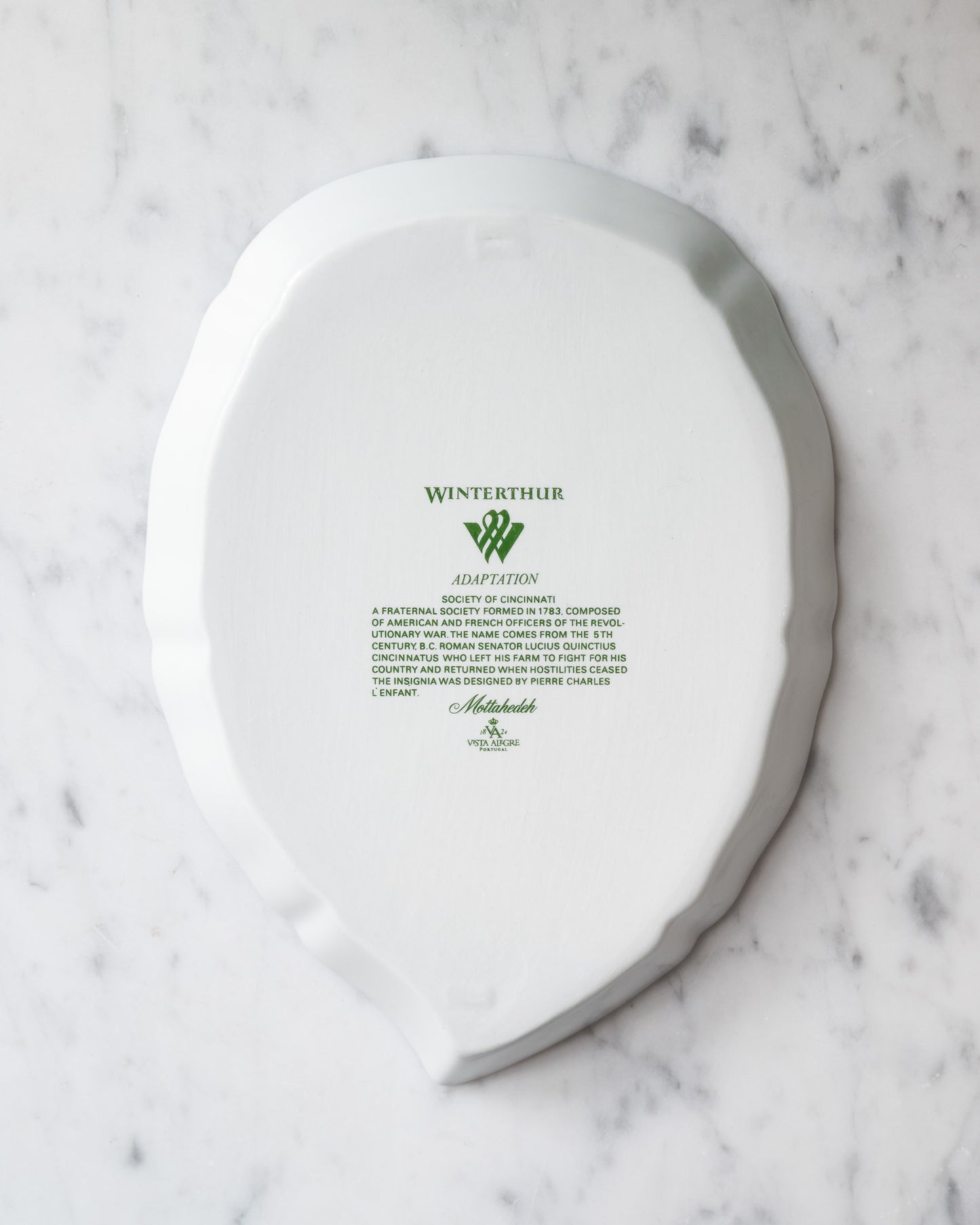 Bottom of a white porcelain leaf-shaped tray with green Winterthur logo and descriptive text