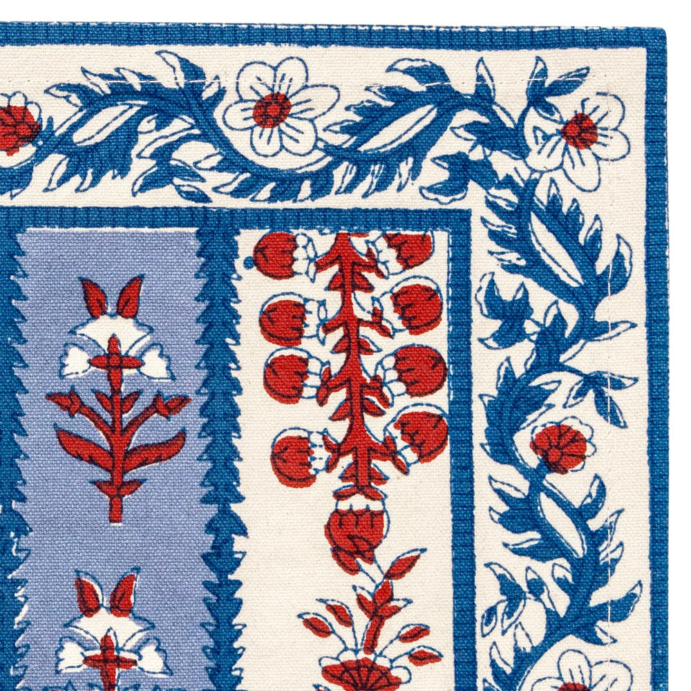 Close up of the corner of a cloth placemat with a blue and off-white striped pattern and decorated with block printed navy blue and red floral motifs laid flat against a white background