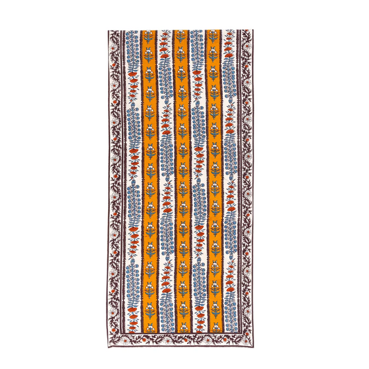 An off-white and mustard yellow striped table runner decorated with block printed mahogany brown, light blue and burnt orange floral motifs against a white background.
