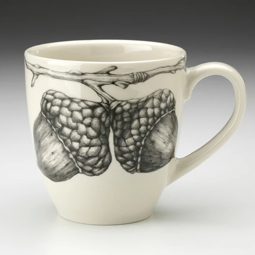 An off-white stoneware tapered mug featuring a sketch of two acorns on a branch in black and a dark brown interior.