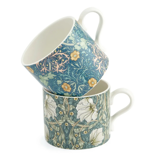 Two William Morris floral-patterned mugs in shades of blues, greens and yellows stacked on a white background