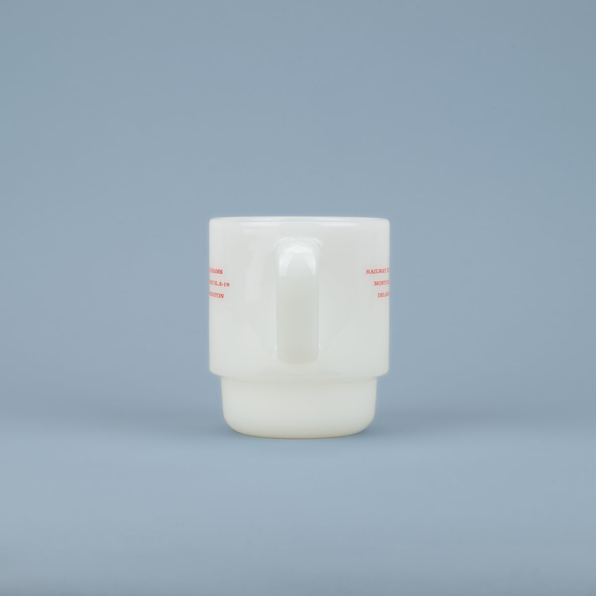 Handle of a white milk glass mug with red lettering on the sides against a blue background