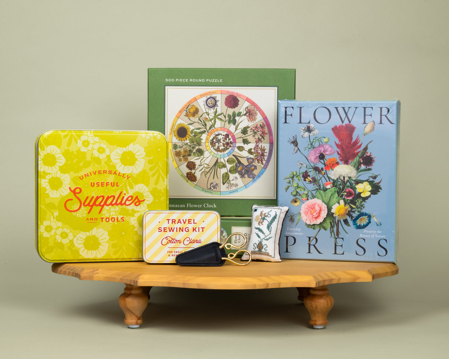 A collection of craft kits, needlework tools, and a floral jigsaw puzzle against a plain green background.