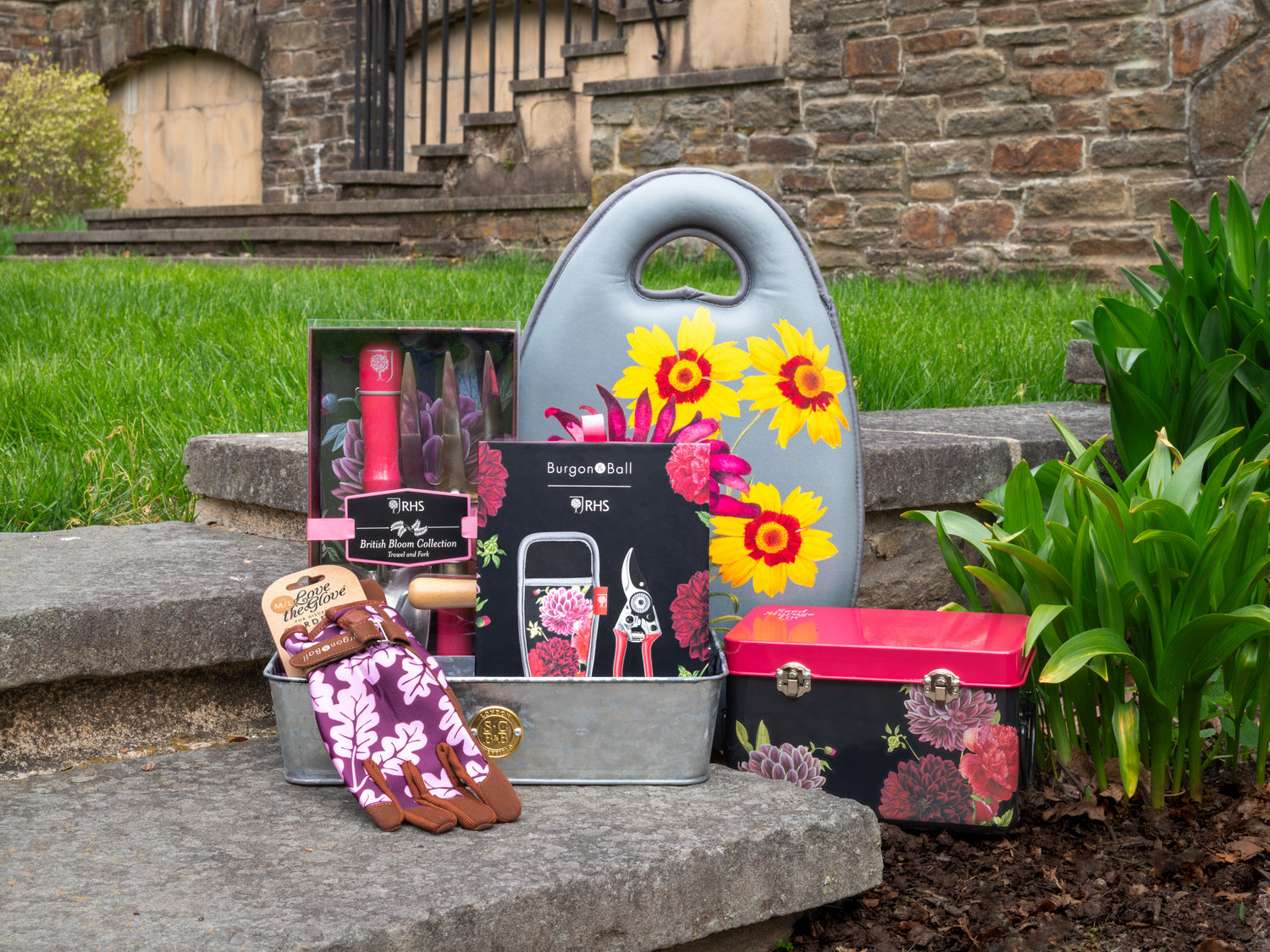 Collection of floral patterned gardening tools and accessories on a stone surface with grass and a stone wall in the background