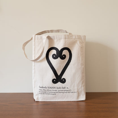 Beige tote bag with black heart design and text on a wooden surface.