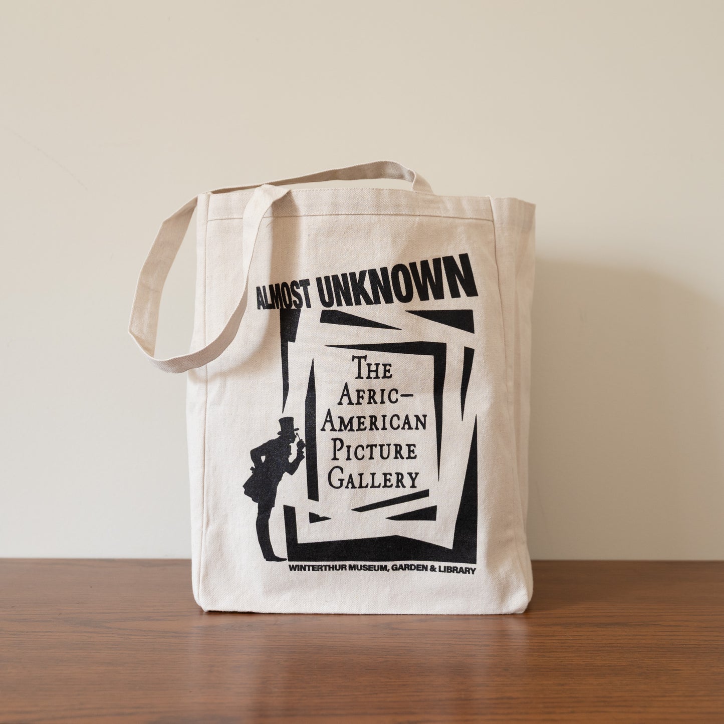 Tote bag with 'Almost Unknown: The African-American Picture Gallery' design on a wooden surface.