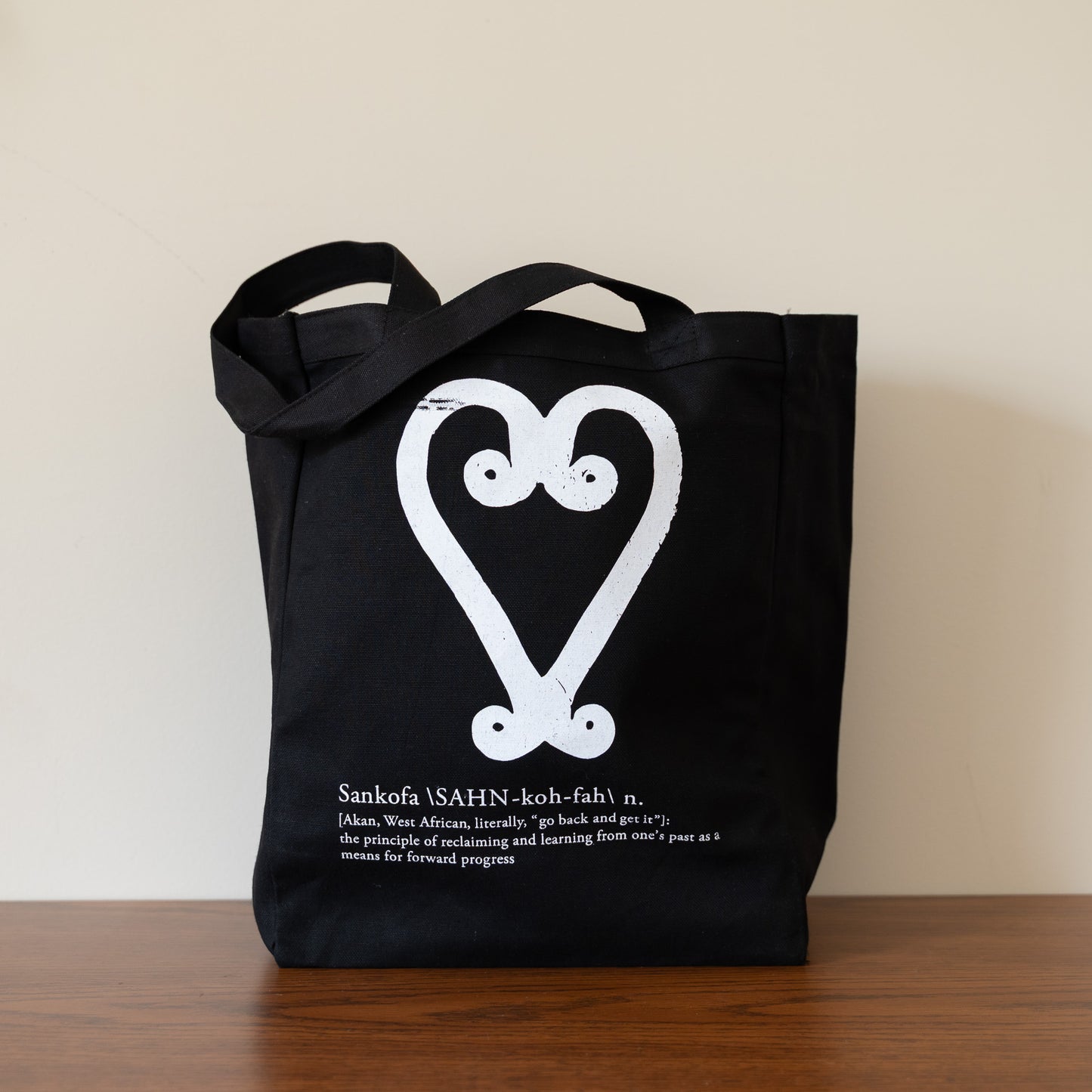 Black tote bag with white design and text on a wooden surface.