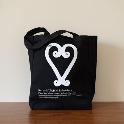 Black tote bag with white design and text on a wooden surface.