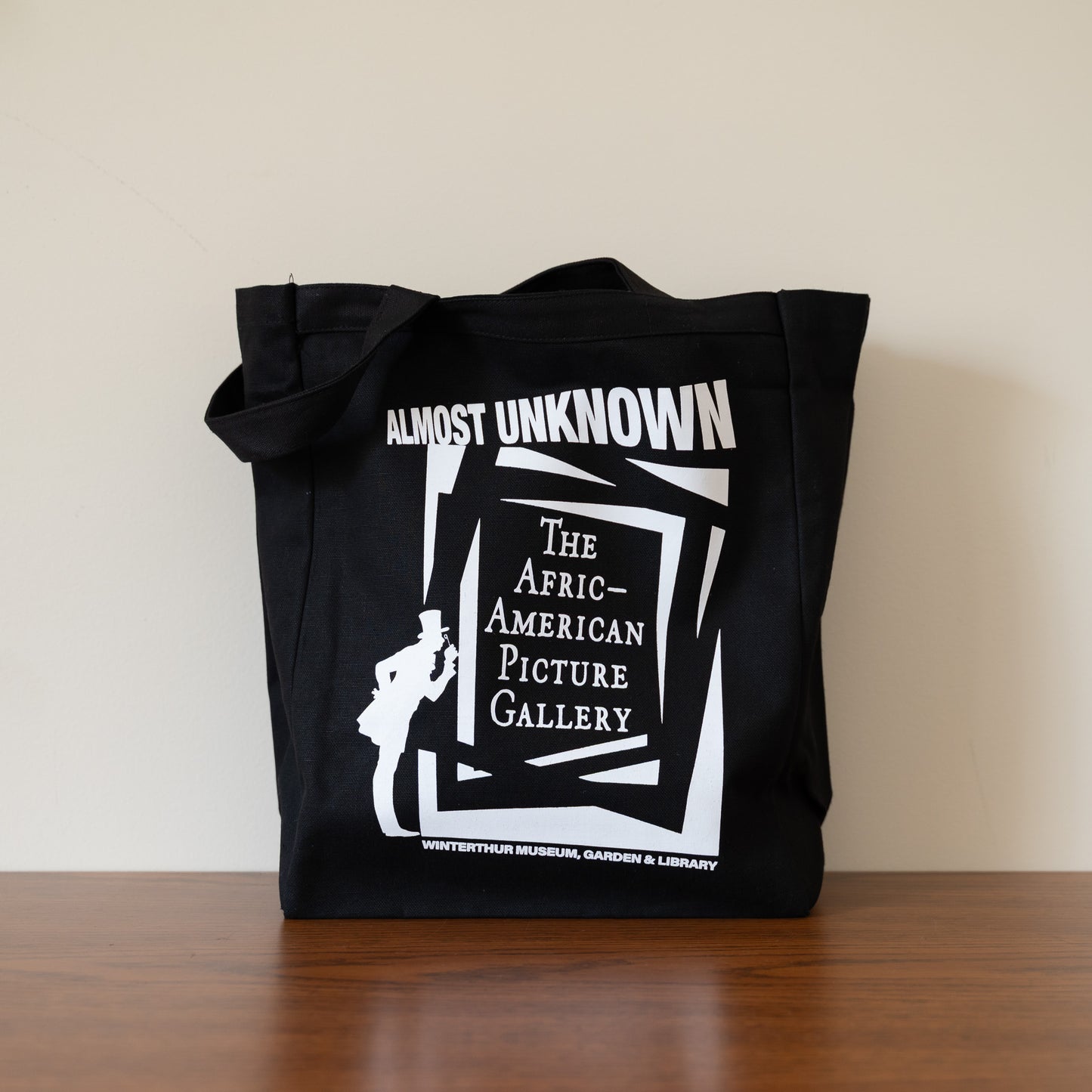 Black tote bag with white graphic and text on a wooden surface