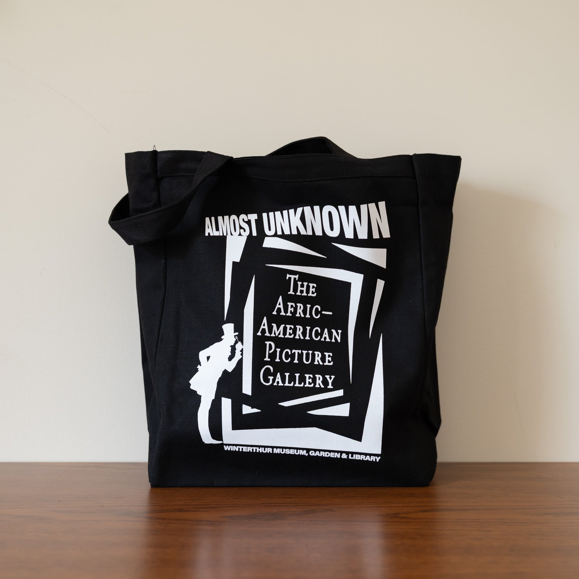 Black tote bag with white graphic and text on a wooden surface