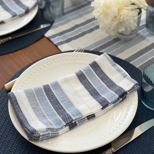 Folded white and blue striped cloth napkin on a white plate with a table setting in the background