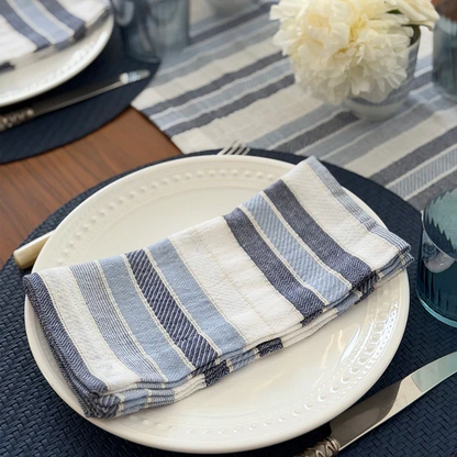 Folded white and blue striped cloth napkin on a white plate with a table setting in the background