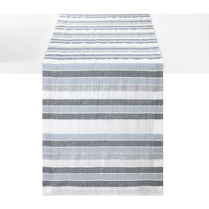 A striped woven cotton table runner with horizontal stripes in shades of blue and white, shown hanging against a white background.