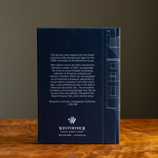 Back cover of a blue journal with architectural history text and Winterthur logo on a wooden tabletop.