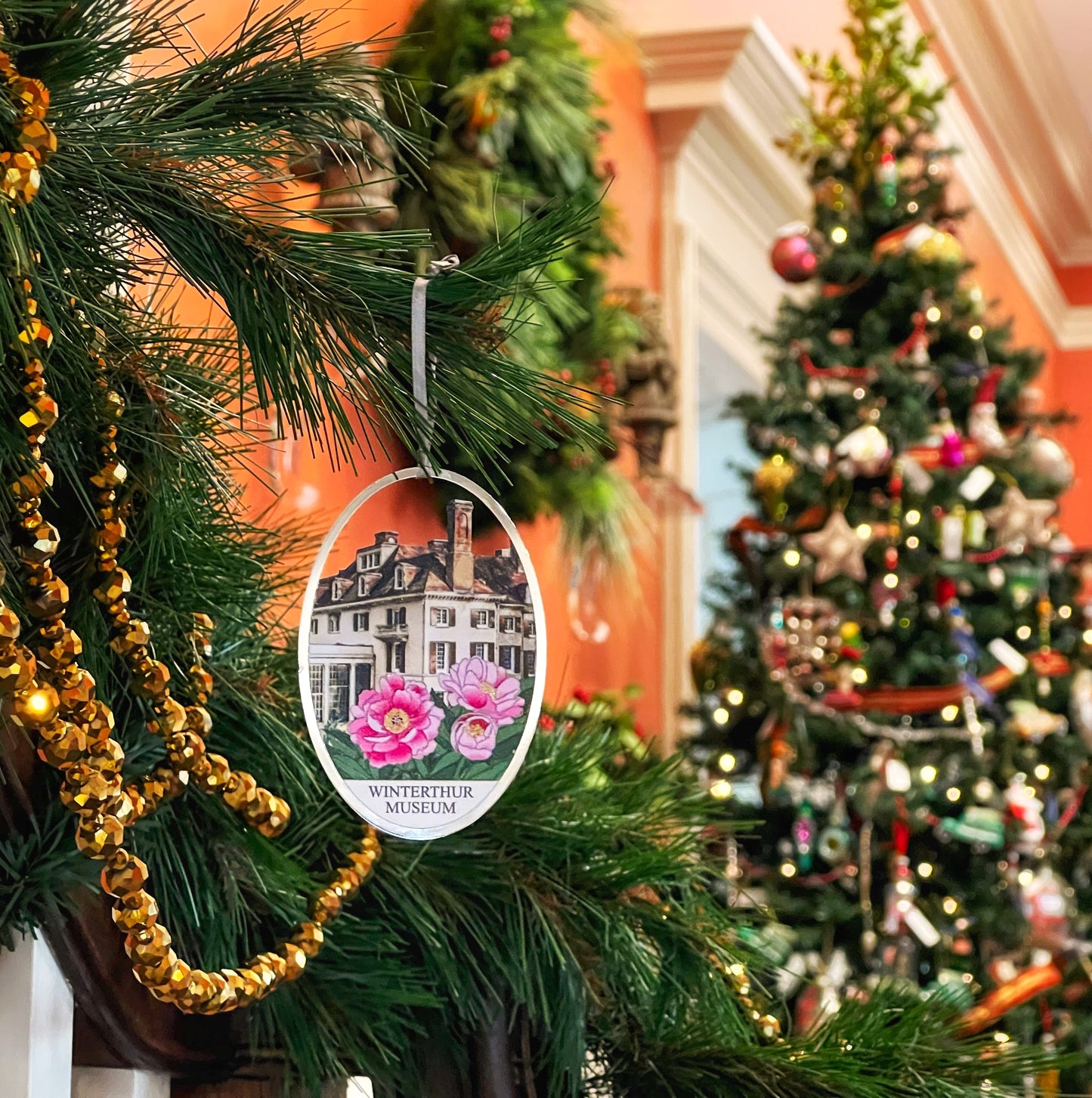 Oval metal ornament featuring a house and pink peony flowers with the words "WINTERTHUR MUSEUM'