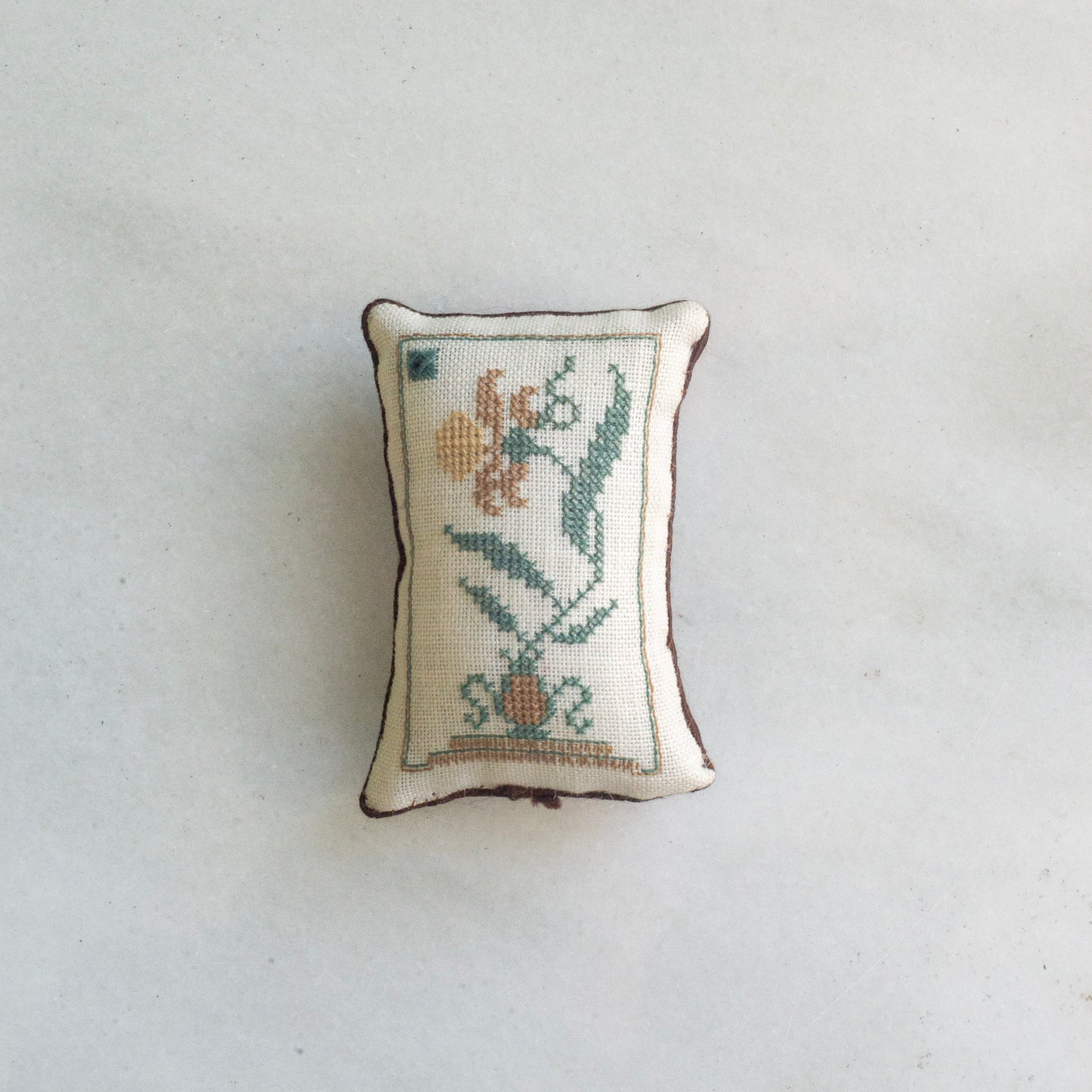 Small ivory colored pincushion with a green and yellow floral design 