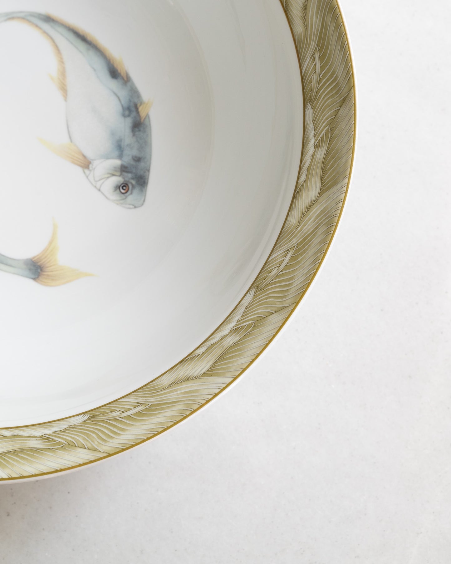 Detail of olive colored outer rim of a white porcelain bowl with a watercolor  blue trout motif.