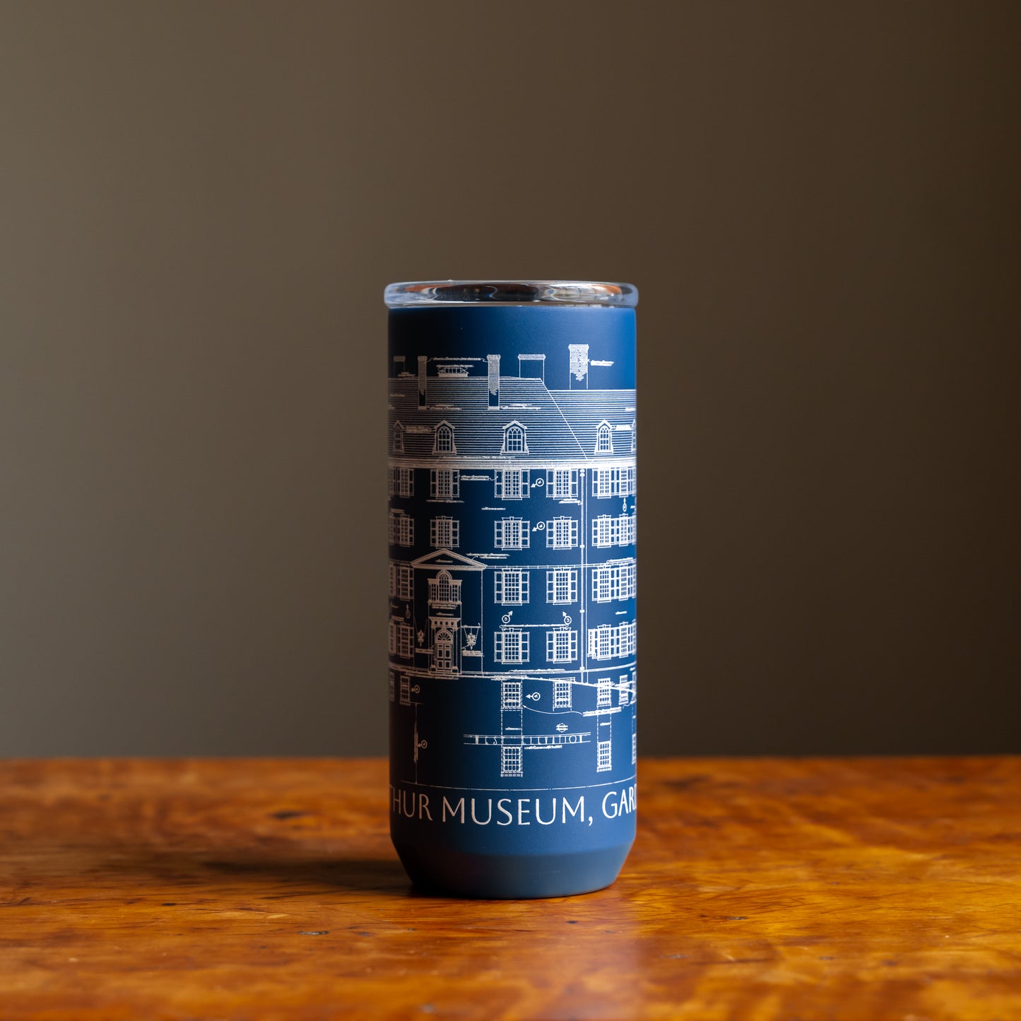 Blue tumbler featuring an architectural sketch and the words "Winterthur Museum, Garden & Library"  under design on a wooden tabletop and dark background