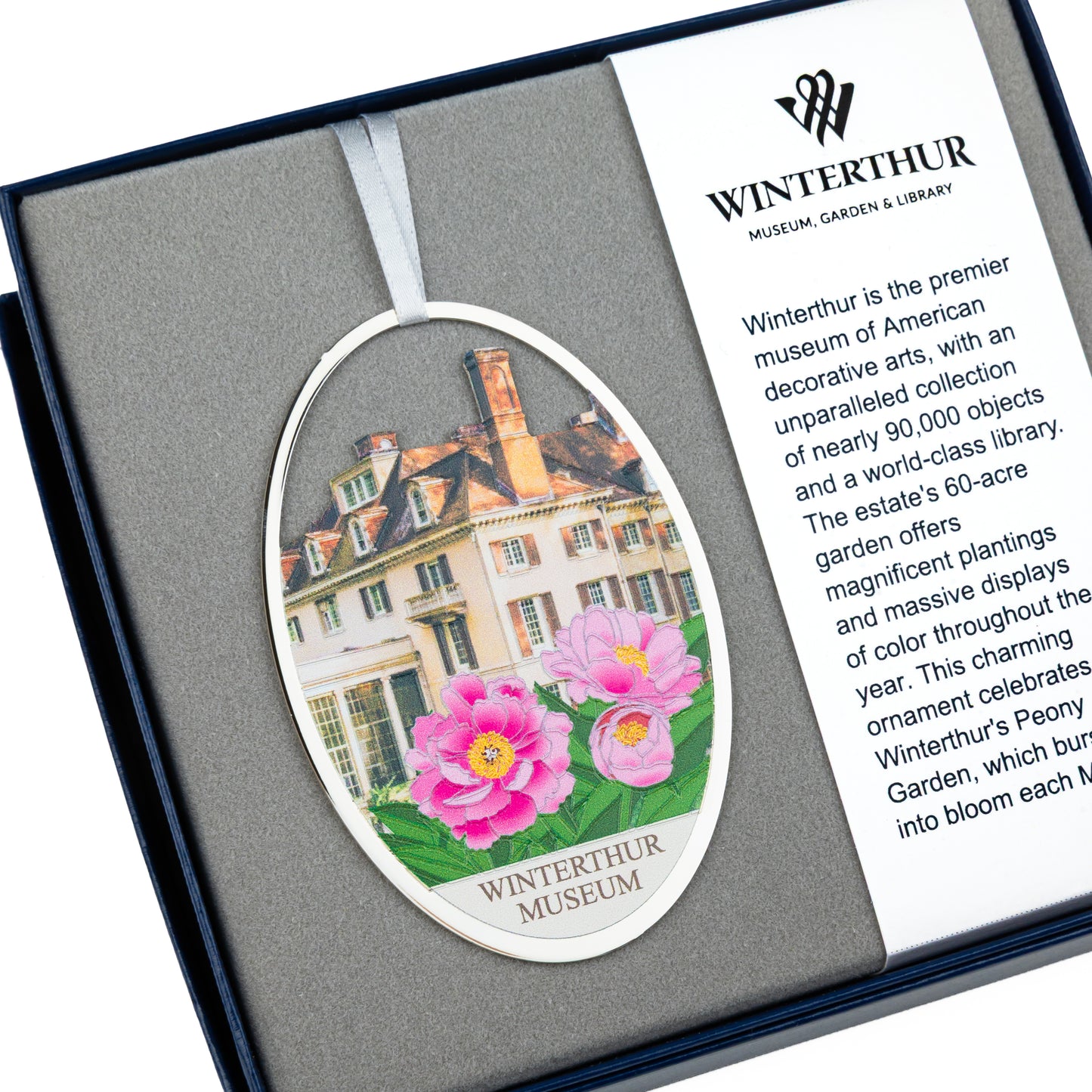 An oval winter tree ornament presented in a dark gift box with a white insert card. The ornament features a printed illustration of Winterthur Museum architecture and bright pink flowers, with the text 'WINTERTHUR MUSEUM' at the bottom.