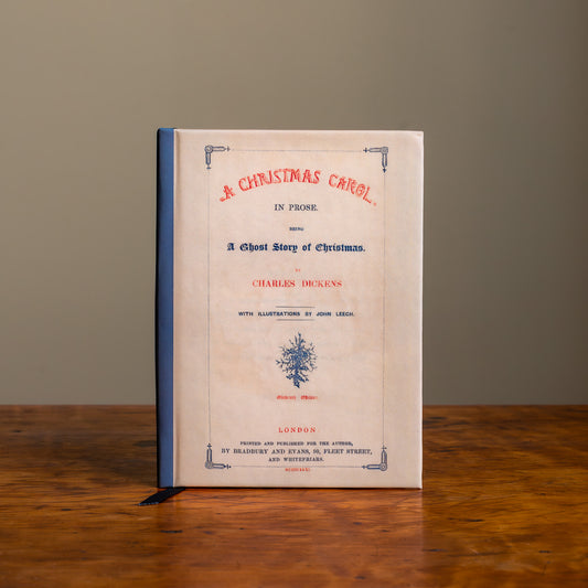 The front cover of a notebook featuring the 1846 title page of A Christmas Carol by Charles Dickens on a wooden tabletop against a plain background