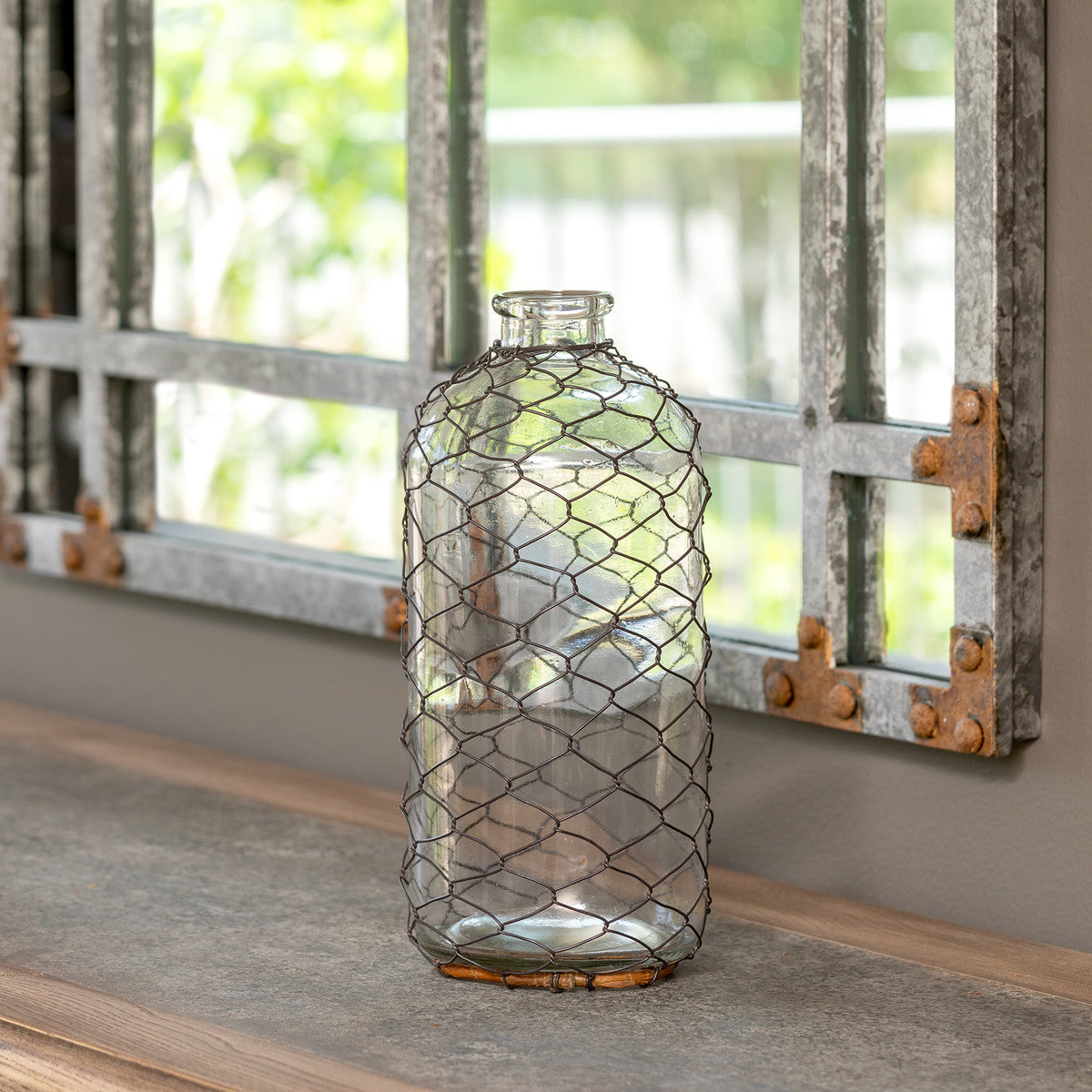 Decorative glass vase with wire mesh design on a windowsill.