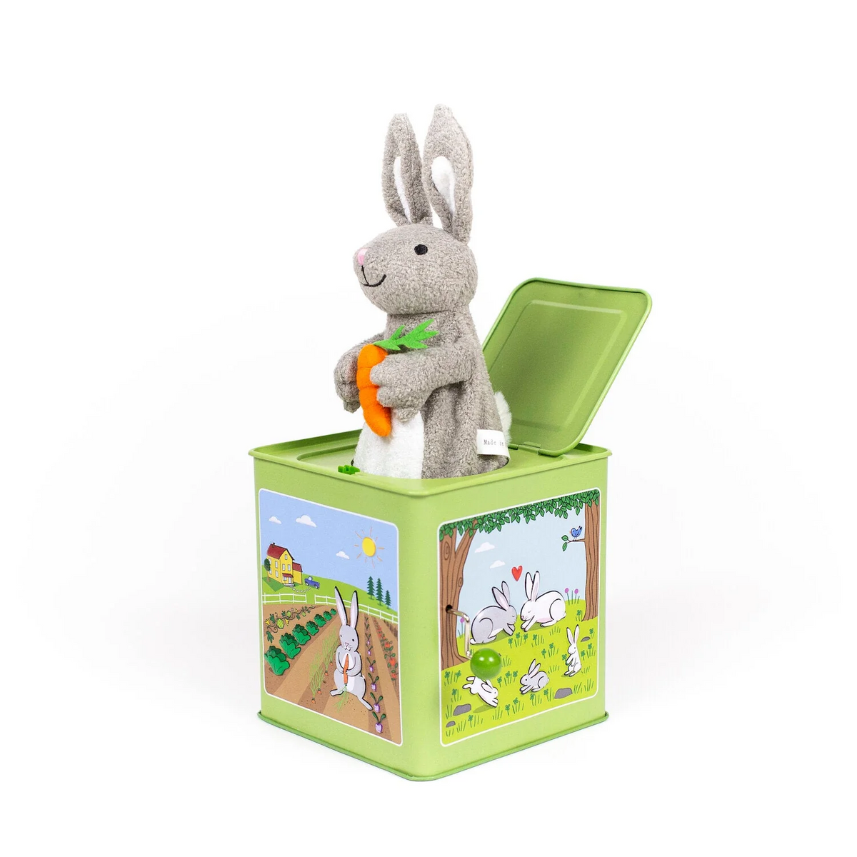 Side view of a green metal jack-in-the-box featuring various bunny pastoral illustrations with a plush gray bunny holding a carrot sticking out of the top.