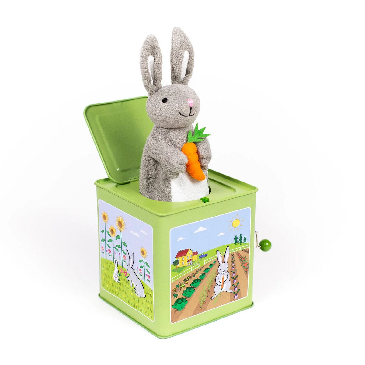 Side view of a green metal jack-in-the-box featuring various bunny pastoral illustrations with a plush gray bunny holding a carrot sticking out of the top.