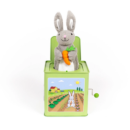 Green metal jack-in-the-box featuring an illustration of a bunny on a farm with a plush gray bunny holding a carrot sticking out of the top.
