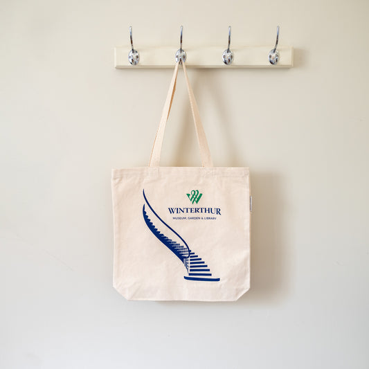Beige tote bag with Winterthur logo and staircase graphic hanging on a wall hook.