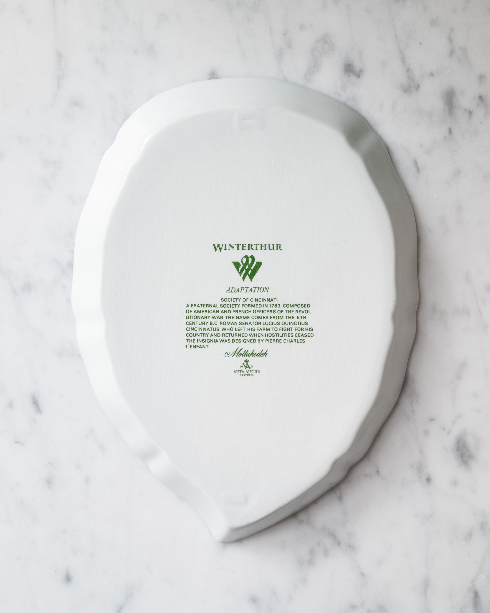 Bottom of a white porcelain leaf-shaped tray with green Winterthur logo and descriptive text