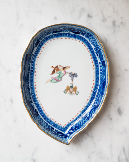 Leaf-shaped porcelain tray featuring an ornate blue border, gold rim, and central motif of a winged woman with a horn and an eagle. 