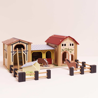 Wooden toy horse stable set with two horses inside on a beige background