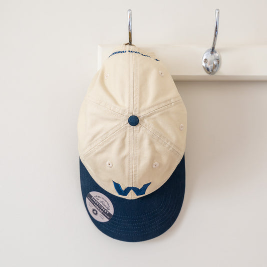 Beige and navy cap with logo on a hook against a white background