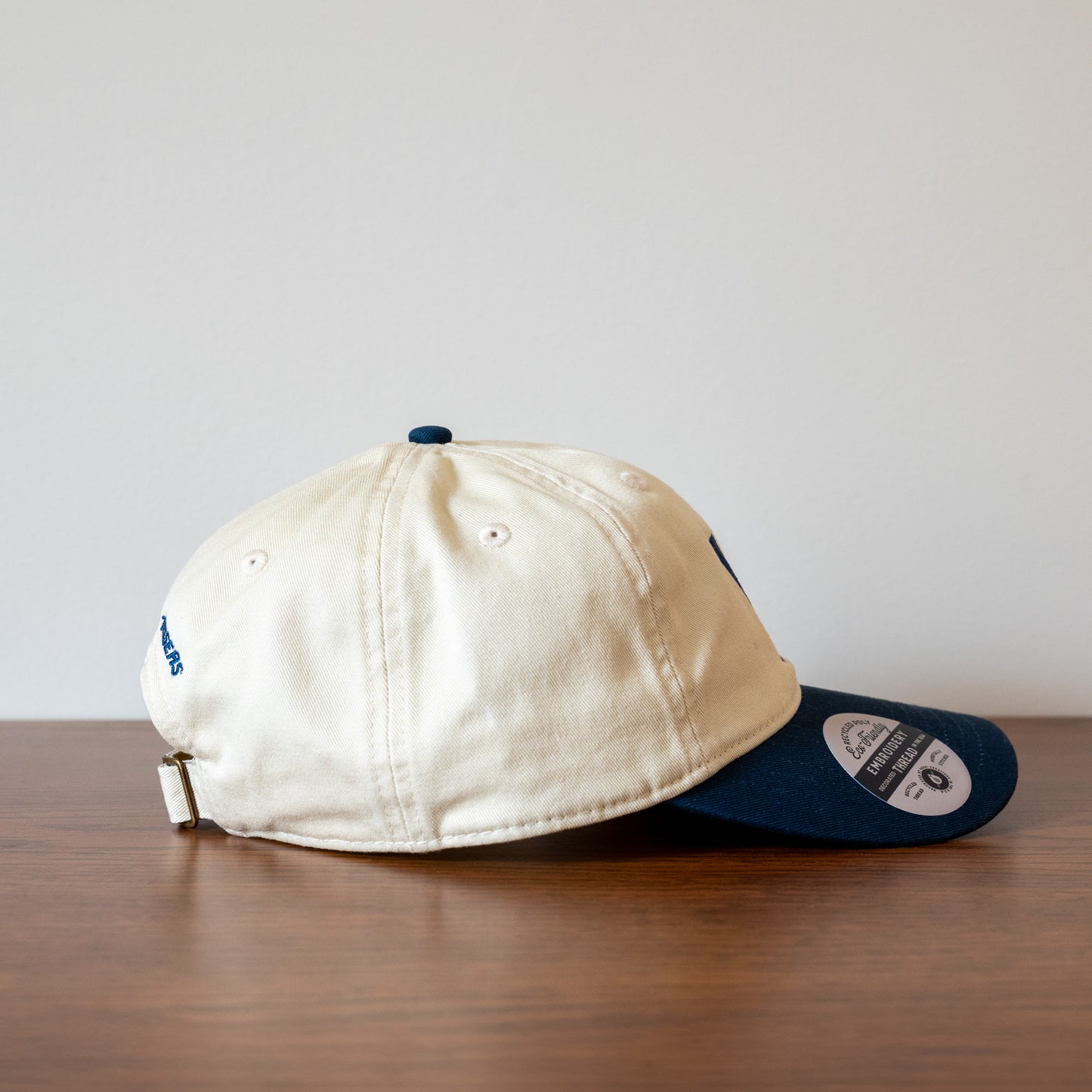 Right side of a beige and blue baseball cap on a wooden surface with a white background