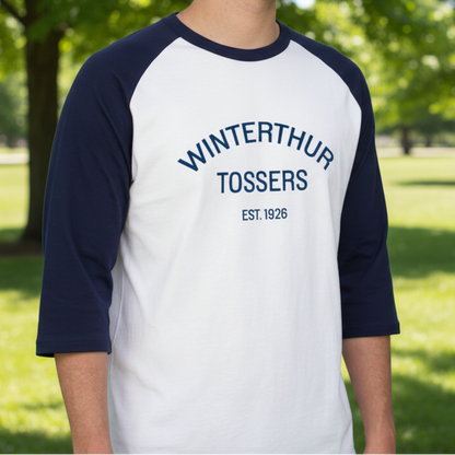 Man wearing a baseball style white t-shirt with navy blue 3/4 sleeves and ring neck collar with the words 'WINTERTHUR TOSSERS EST. 1926' printed in navy blue across the chest 