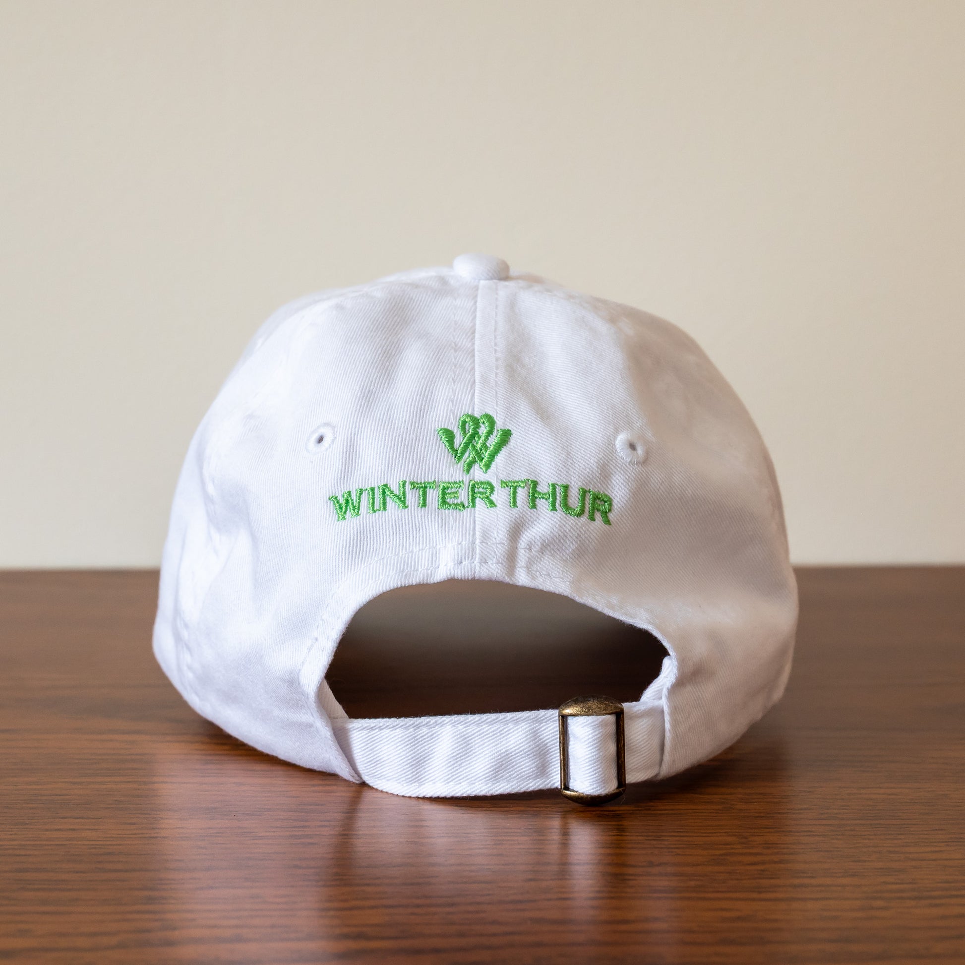 Back of a white baseball cap with the Winterthur logo in green and an adjustable strap with a gold-tone buckle