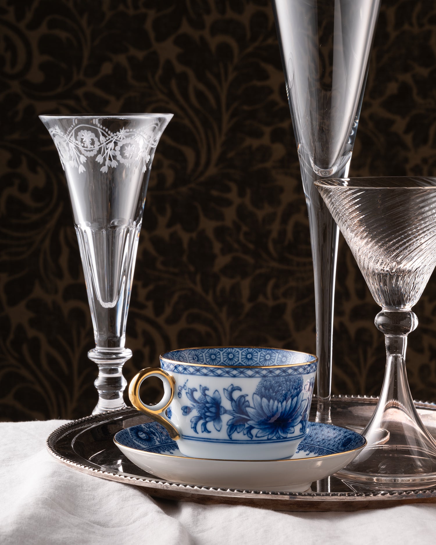 Display of crystal glassware and a teacup on a tray with a dark patterned background