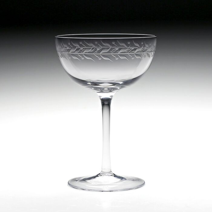 Clear crystal coup glass featuring an engraved vining leaf design around the top rim against a black to white gradient background.