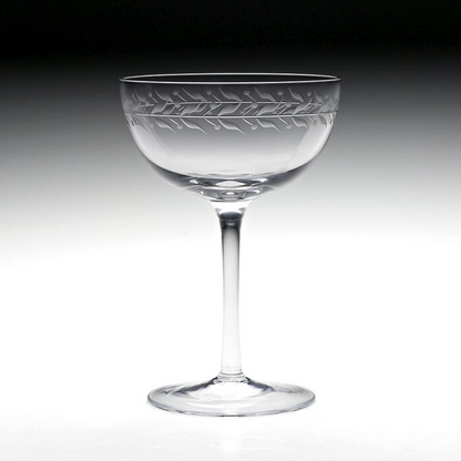 Clear crystal coup glass featuring an engraved vining leaf design around the top rim against a black to white gradient background.