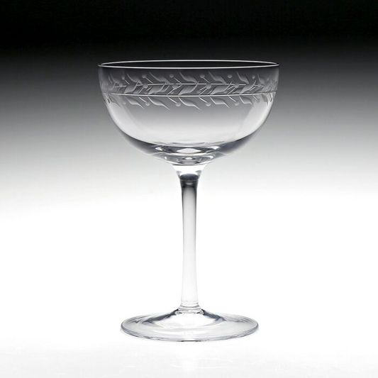 Clear crystal coup glass featuring an engraved vining leaf design around the top rim against a black to white gradient background.