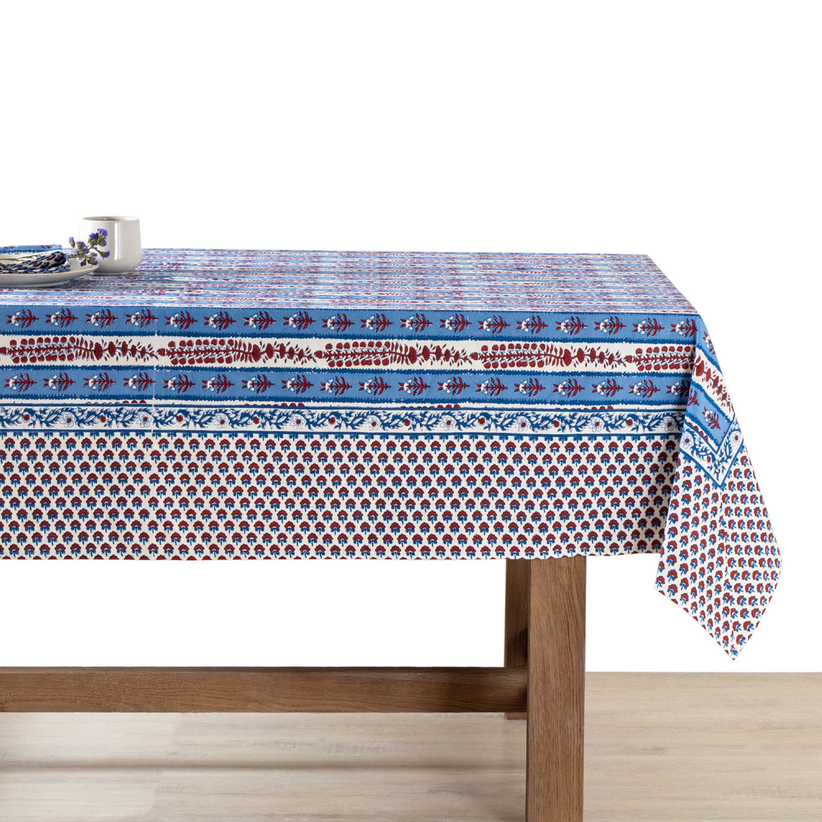 Block-printed tablecloth with white and blue stripes decorated with red floral motifs and a wide floral border draped over a wooden table with a white background