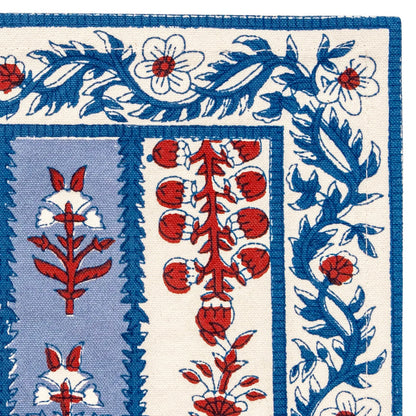 Close up of the corner of a cloth placemat with a blue and off-white striped pattern and decorated with block printed navy blue and red floral motifs laid flat against a white background