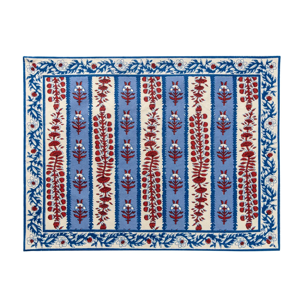 Rectangular cloth placemat with a blue and off-white striped pattern and decorated with block printed navy blue and red floral motifs laid flat against a white background