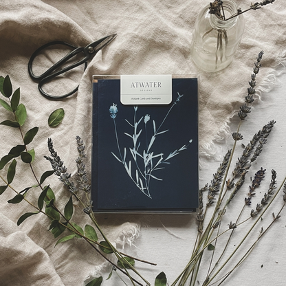 Blue and white botanical notecard set packaged in a clear box and surrounded by plants and garden sheers on a linen cloth